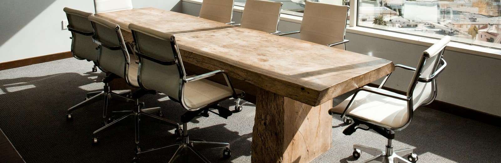 A meeting room with a wooden table and windows along one wall.